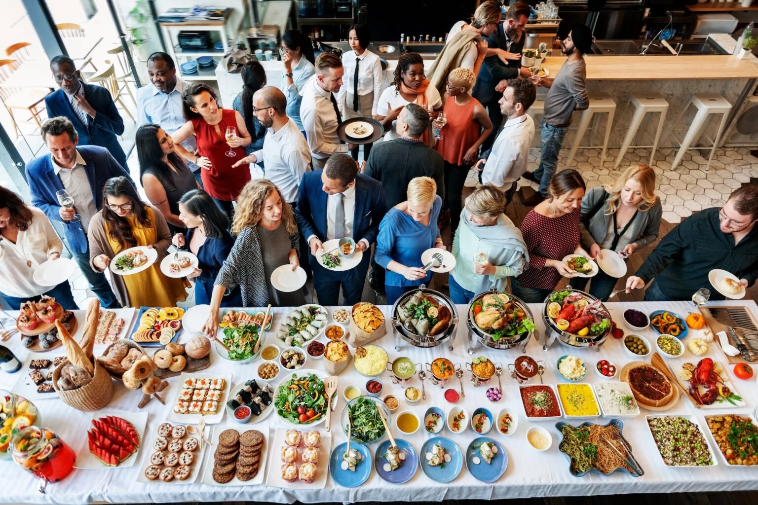 Guests gathering around an abundant catered spread of sandwiches, salads, fruit, and small bites