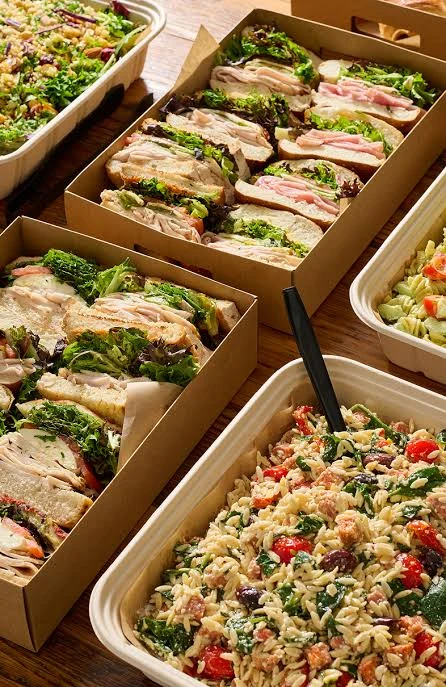 Shared catering boxes of sandwiches alongside generous prepared salads
